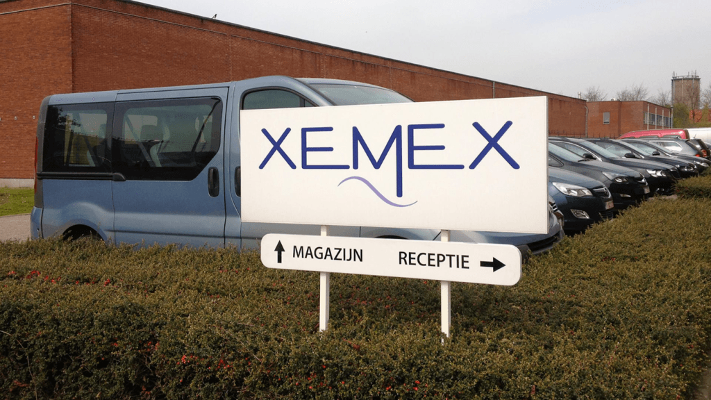 wit wegwijzerbord met blauwe letters naar "Xemex", magazijn en receptie, op industrieterrein