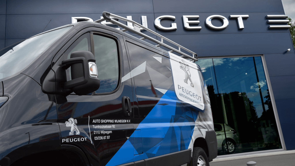 3D-logo met letters van Peugeot en daarvoor zwarte wagen met voertuigreclame voor Peugeot 